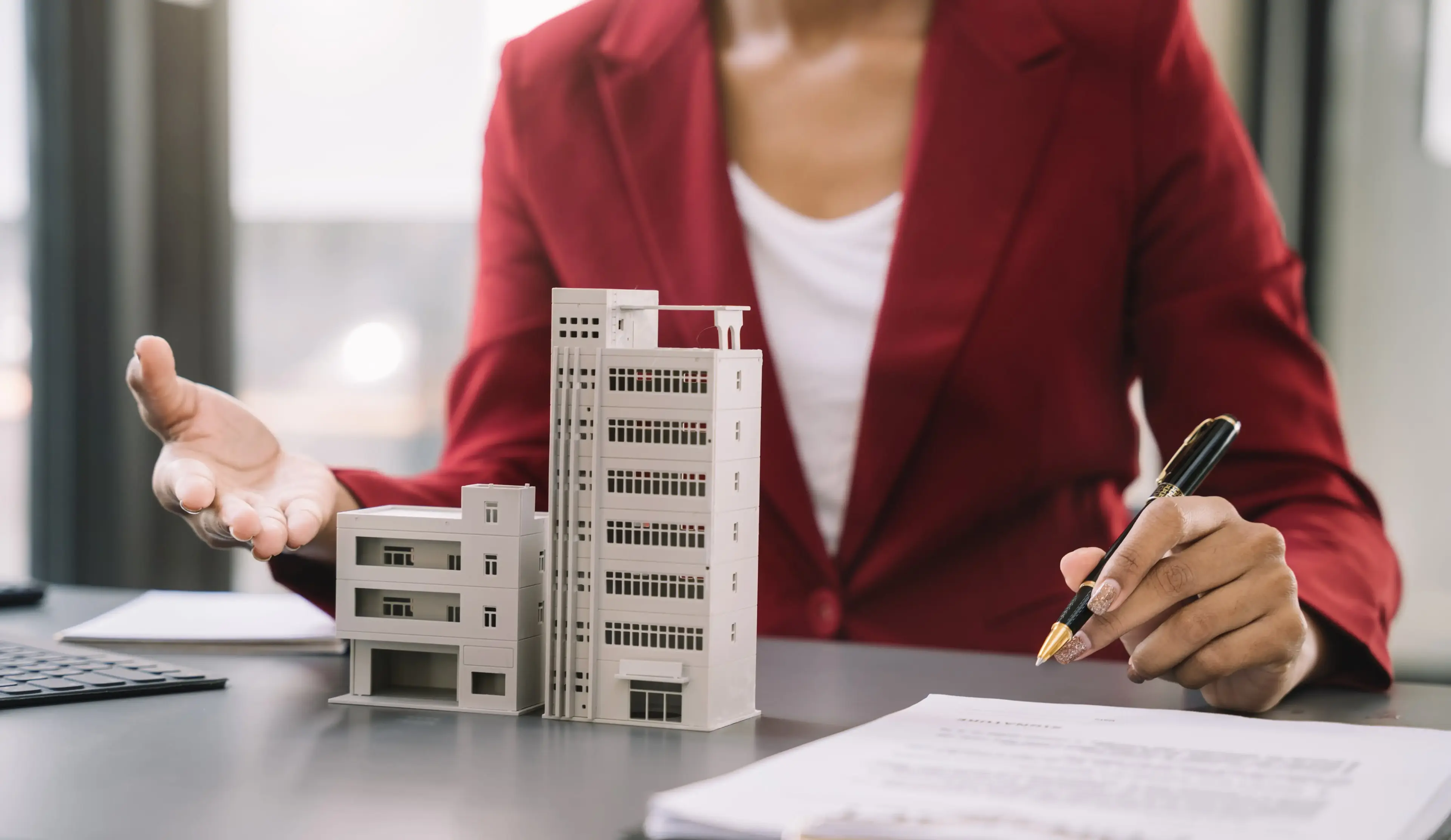 Professional in a red blazer holding a model of a commercial building, depicting commercial lending services.