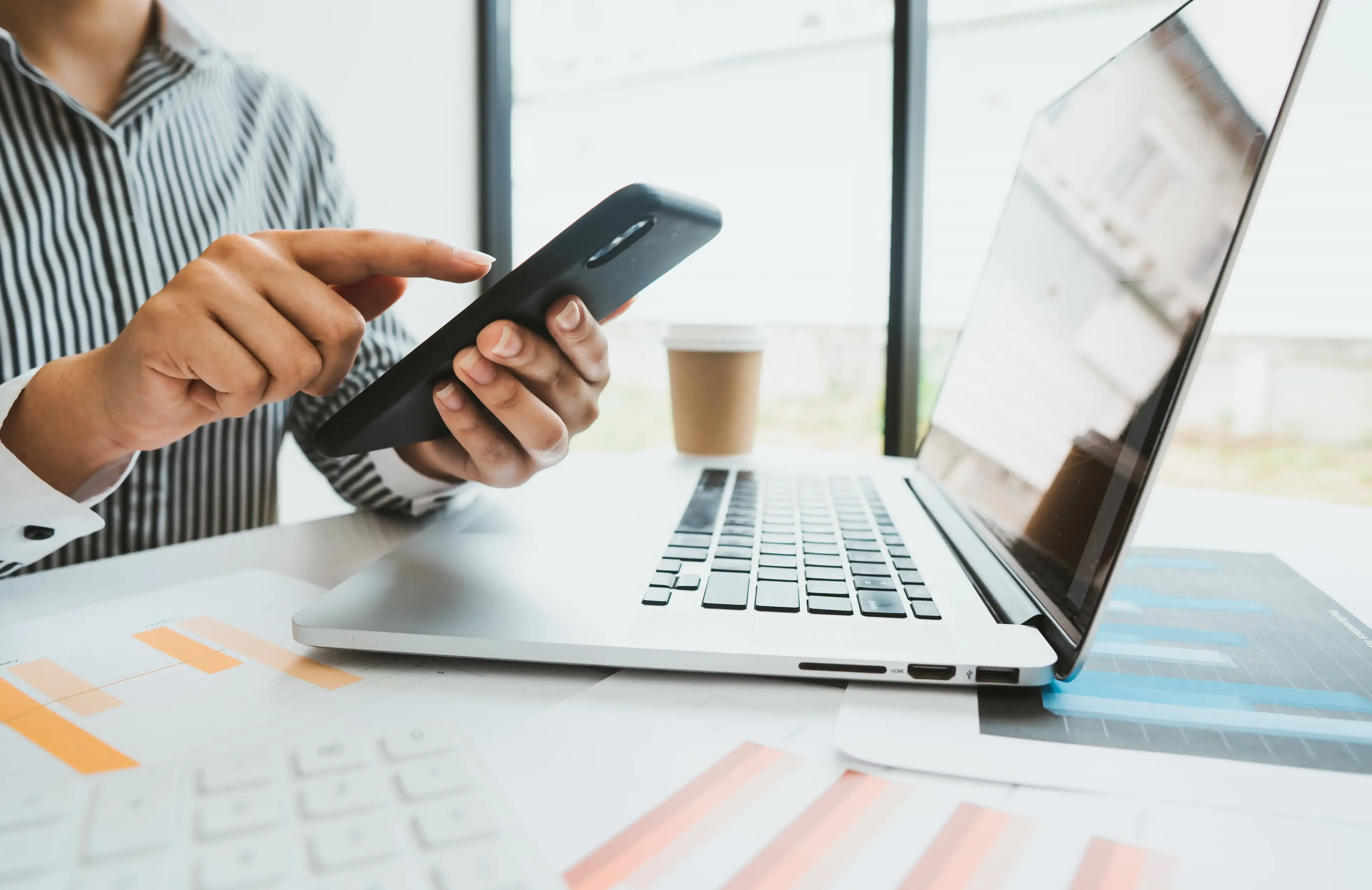 Man holding phone typing in front of laptop.