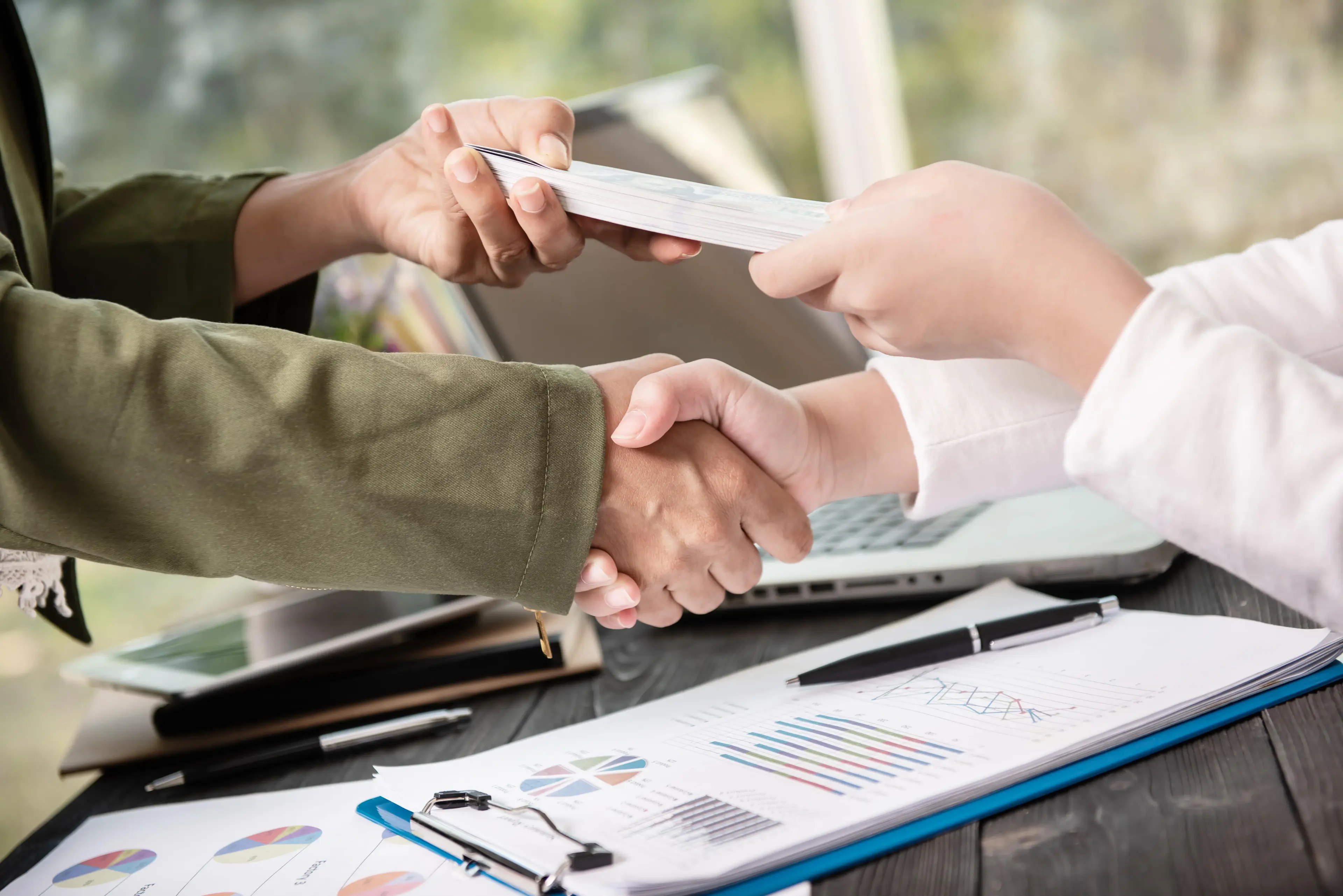 Two people shaking hands with documents and charts in the foreground, illustrating private lending agreements.