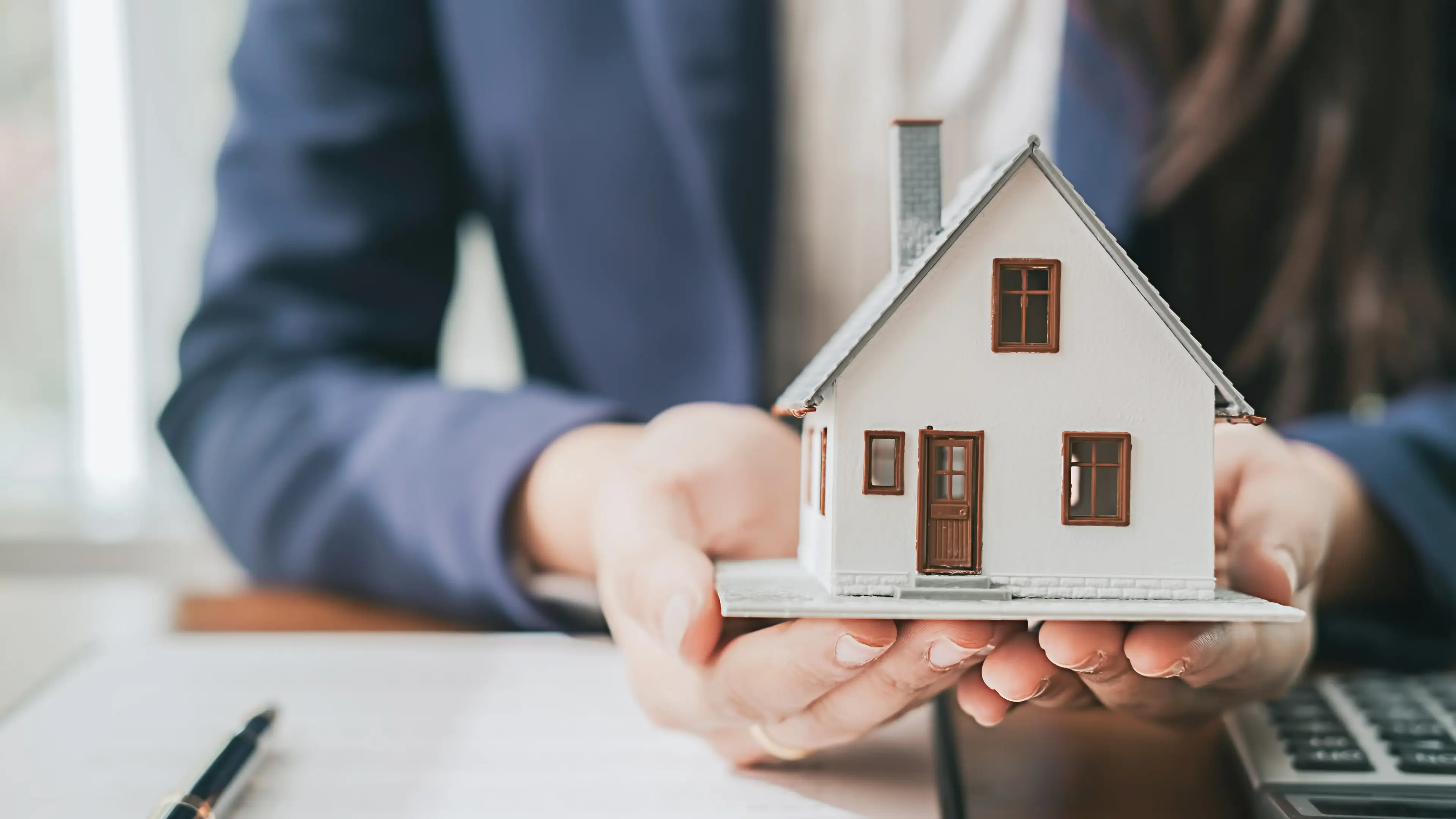 Close-up of a person in a suit holding a model house, representing residential lending services.